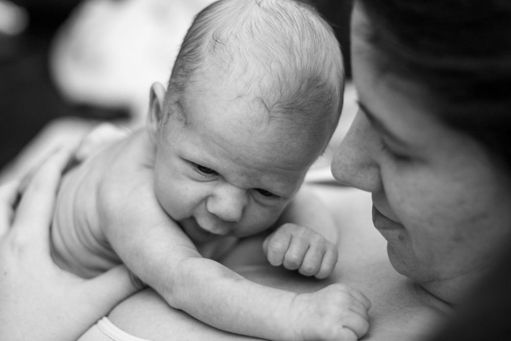 Mother admiring her newborn son laying on her chest.