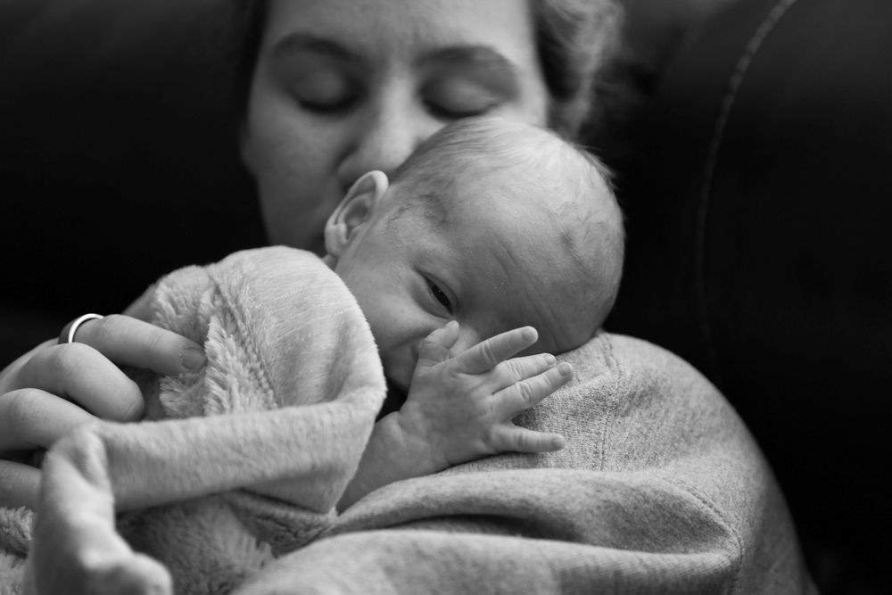 Newborn looking his his hand while laying on his mothers chest.