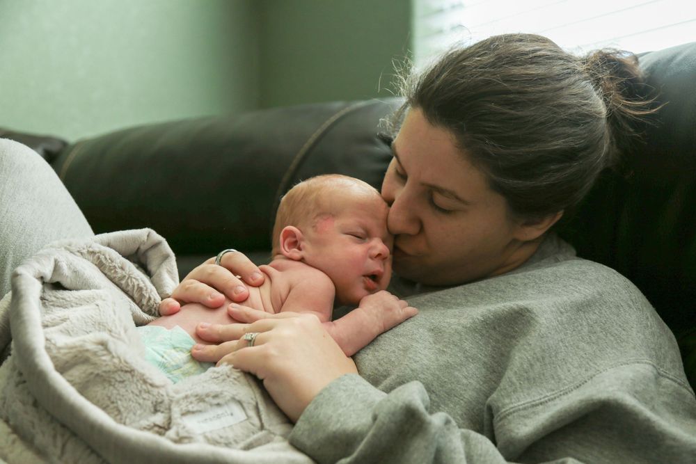 Mother kissing her newborn laying on her chest.