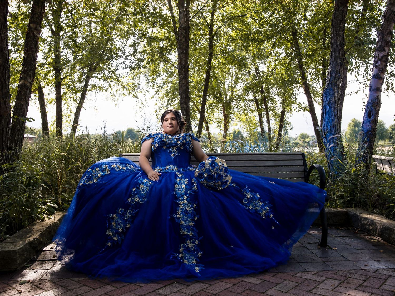 Quinceañera in royal blue dress sitting in a Lake County park. Professional XV photography by Alex T Photography in Waukegan and Mundelein.