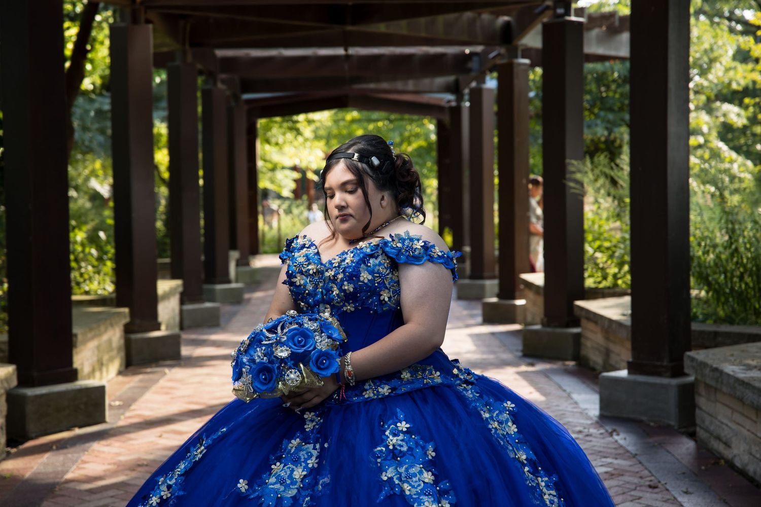 Close-up of Quinceañera in blue dress holding a bouquet under a pergola. Elegant XV portraits at Independence Grove by Alex T Photography.