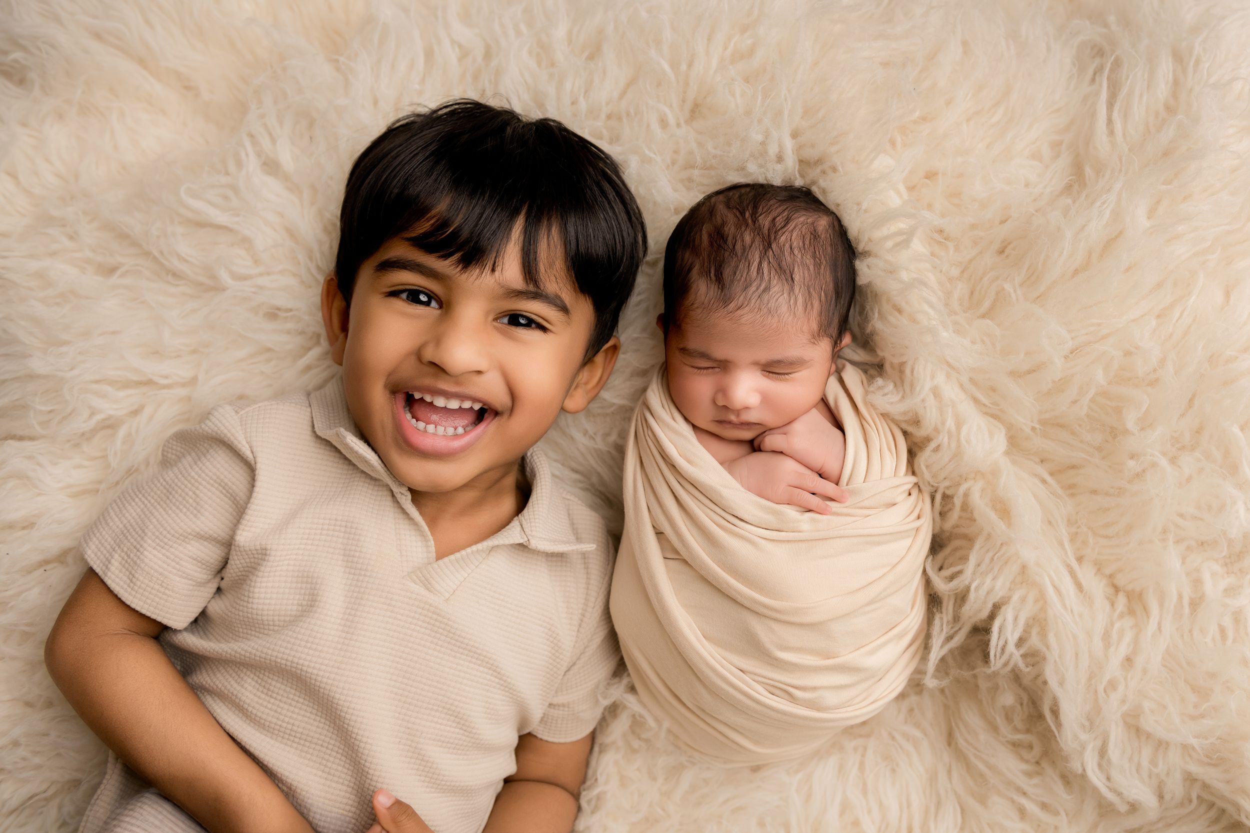 Toddler smiling with his newborn baby brother in a newborn and family photography session.