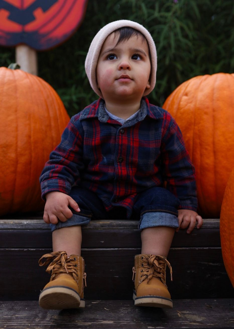 A child with boots sits beside colorful pumpkins in autumn, shown in four similar photos.
