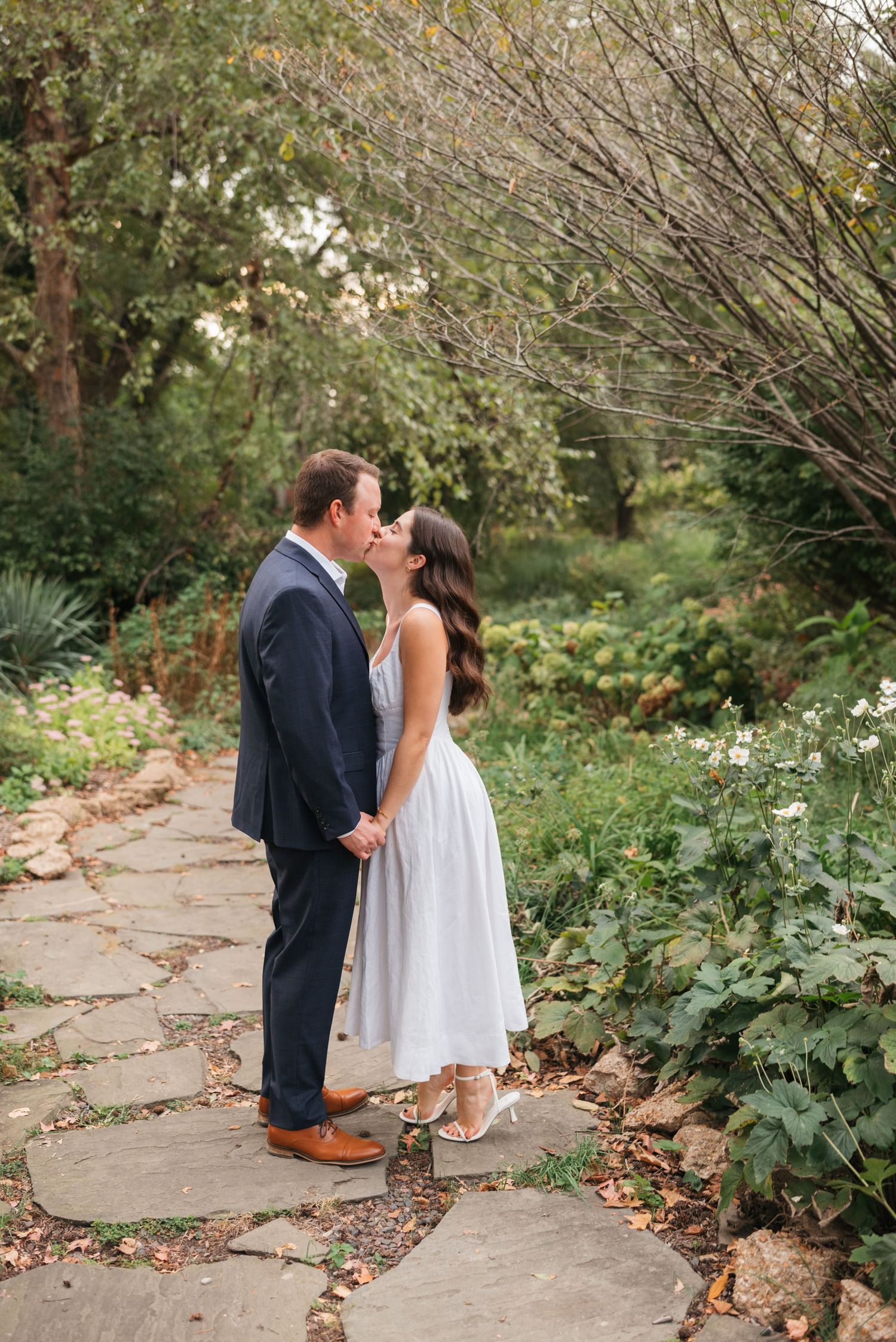 Couple shares romantic moments on stone pathway surrounded by lush greenery.
