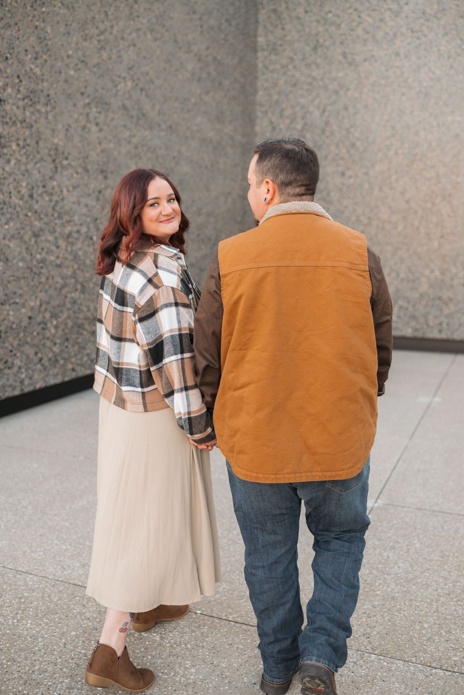 A couple walks together wearing casual fall attire on concrete steps.