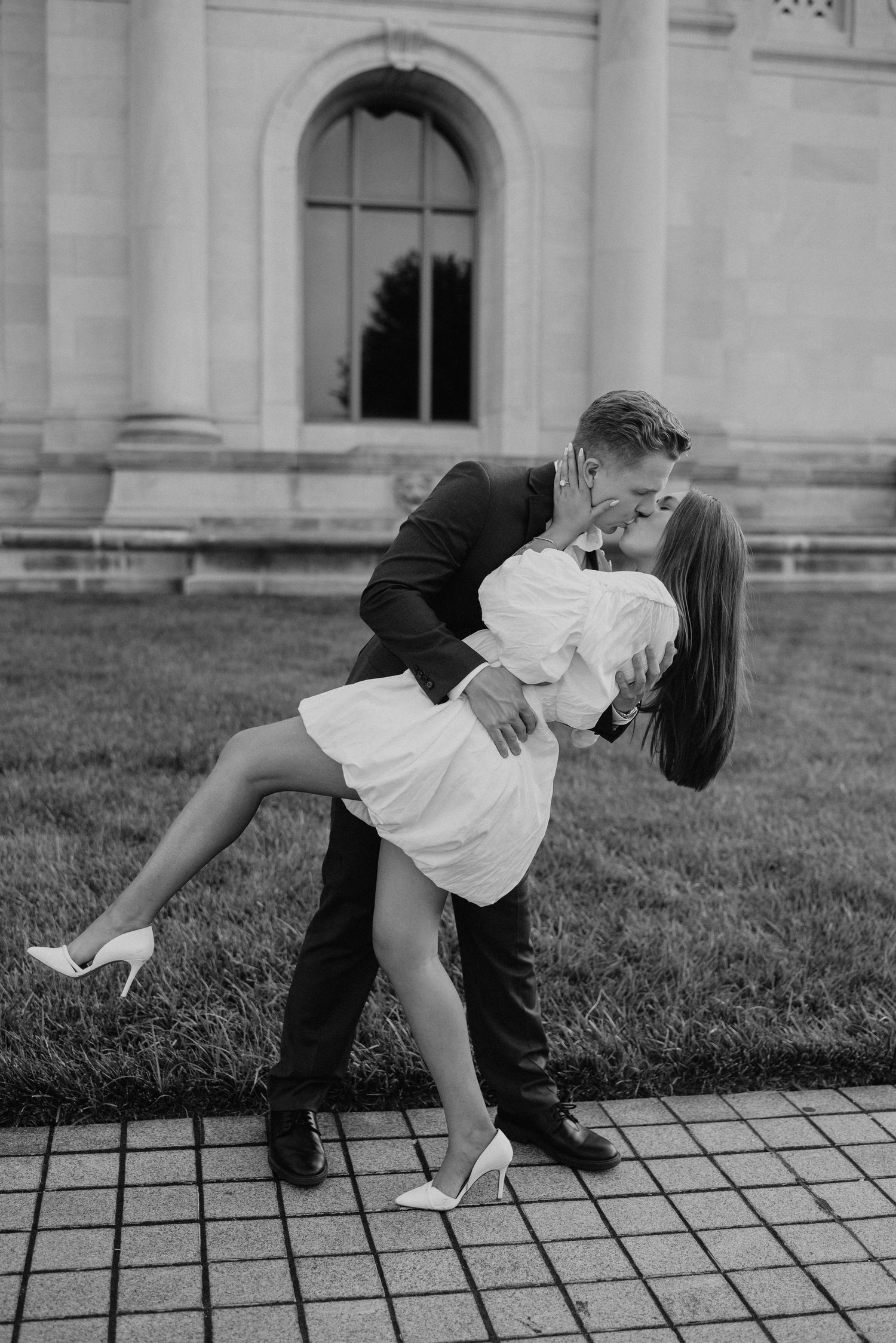 A romantic dip pose between a couple on a paved path near a classical building.