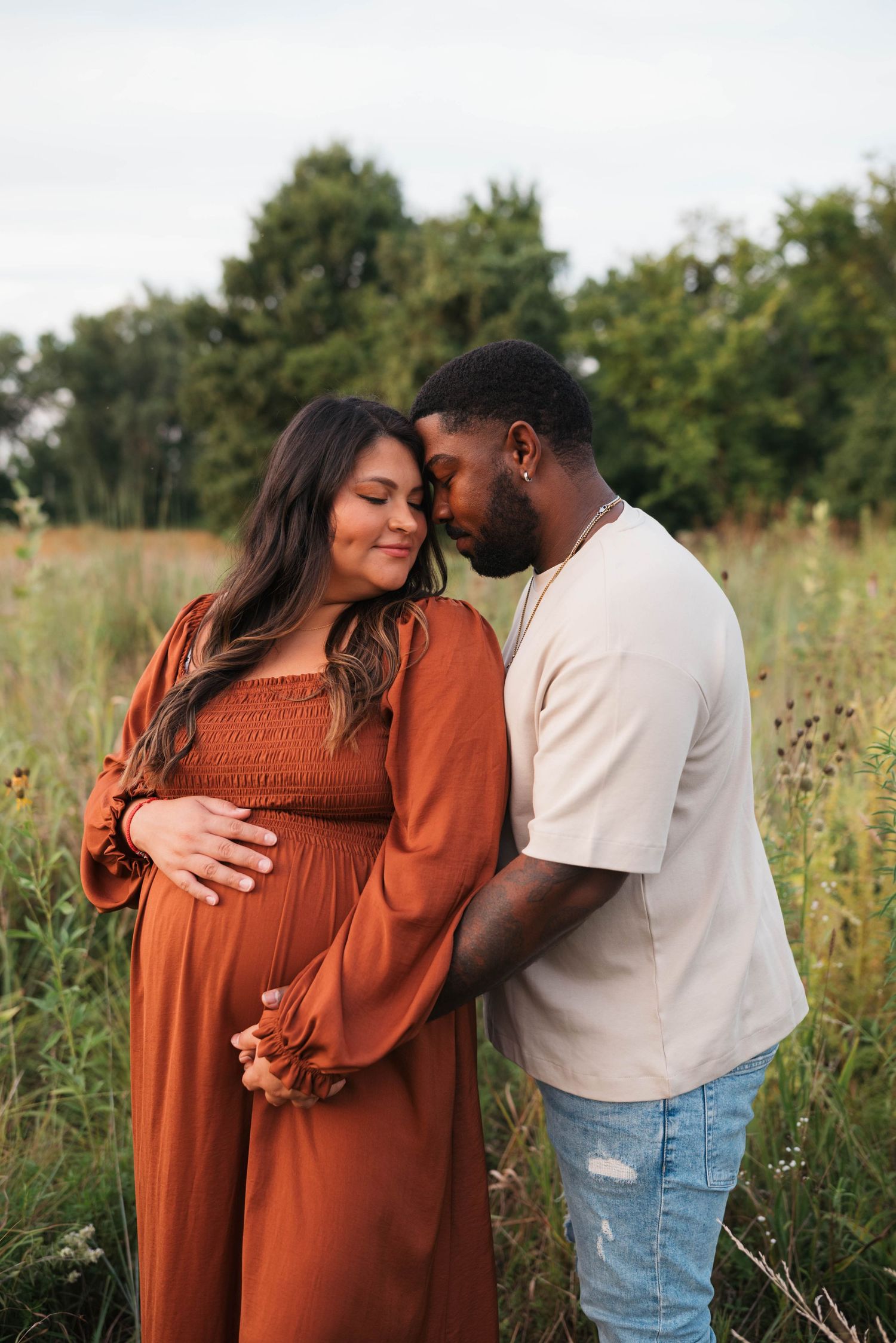 Intimate moment between couple during outdoor maternity session in rustic field.