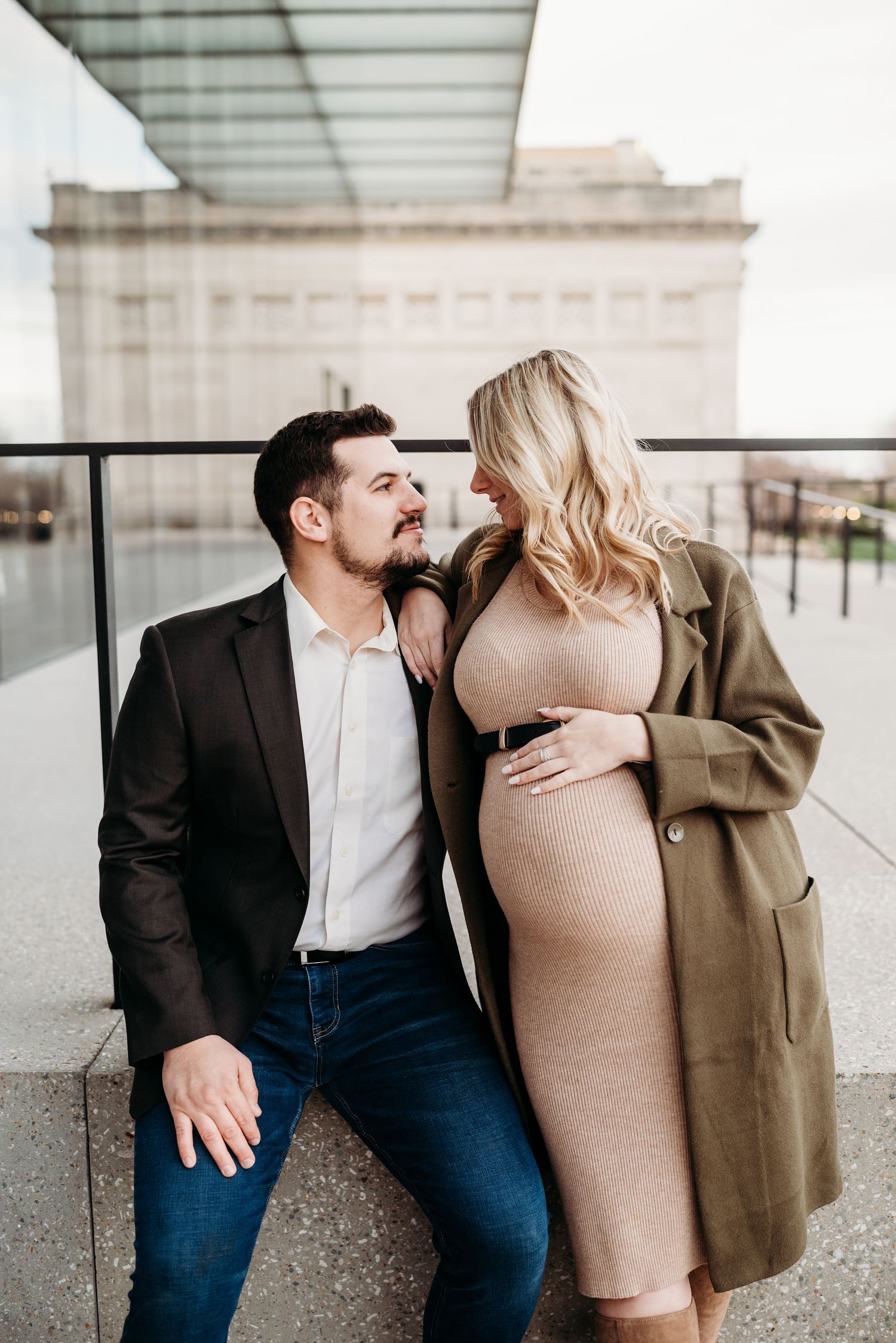 A couple poses together on a modern building balcony in casual formal attire.