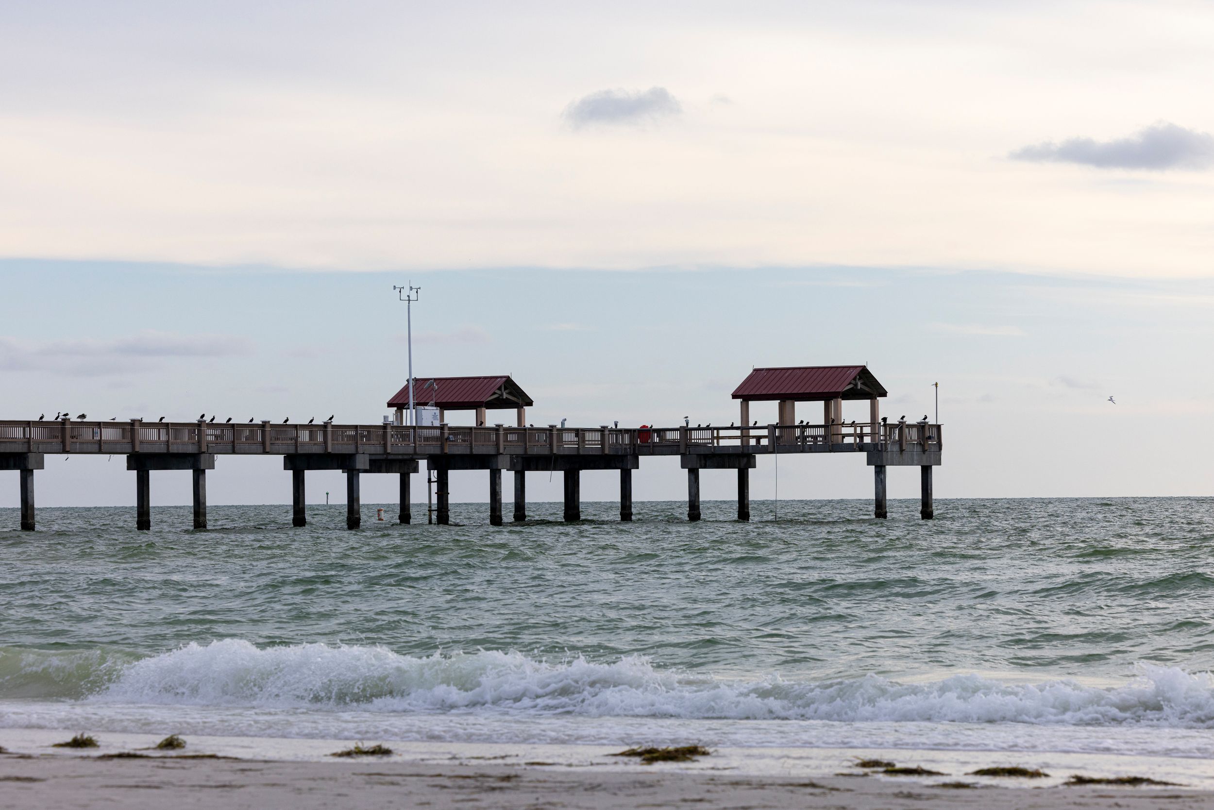 Two wooden pier shelters extend over calm ocean waters against a cloudy sky at sunset.