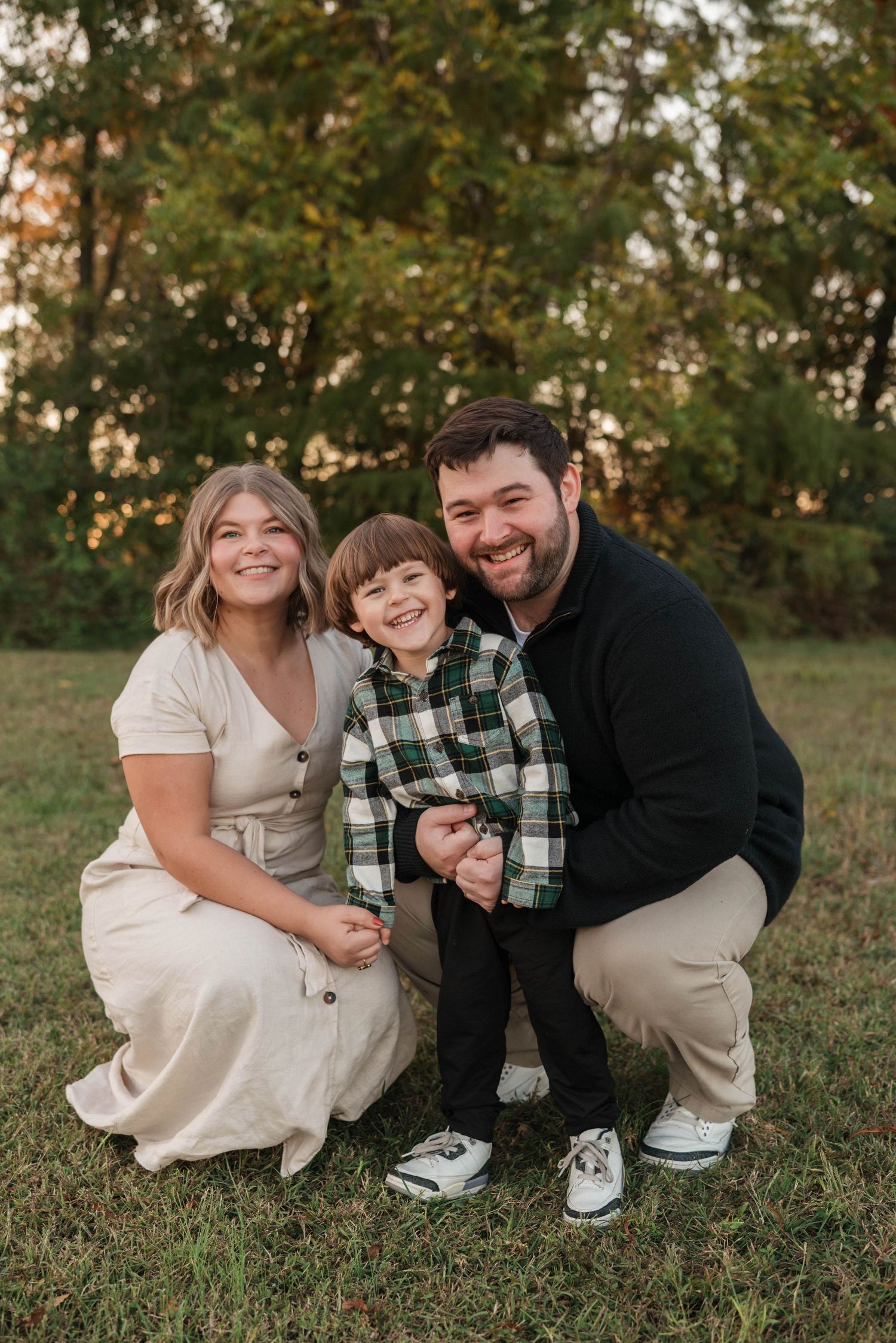 A family of three shares joyful candid moments together while posing on grass during an outdoor autumn photoshoot.