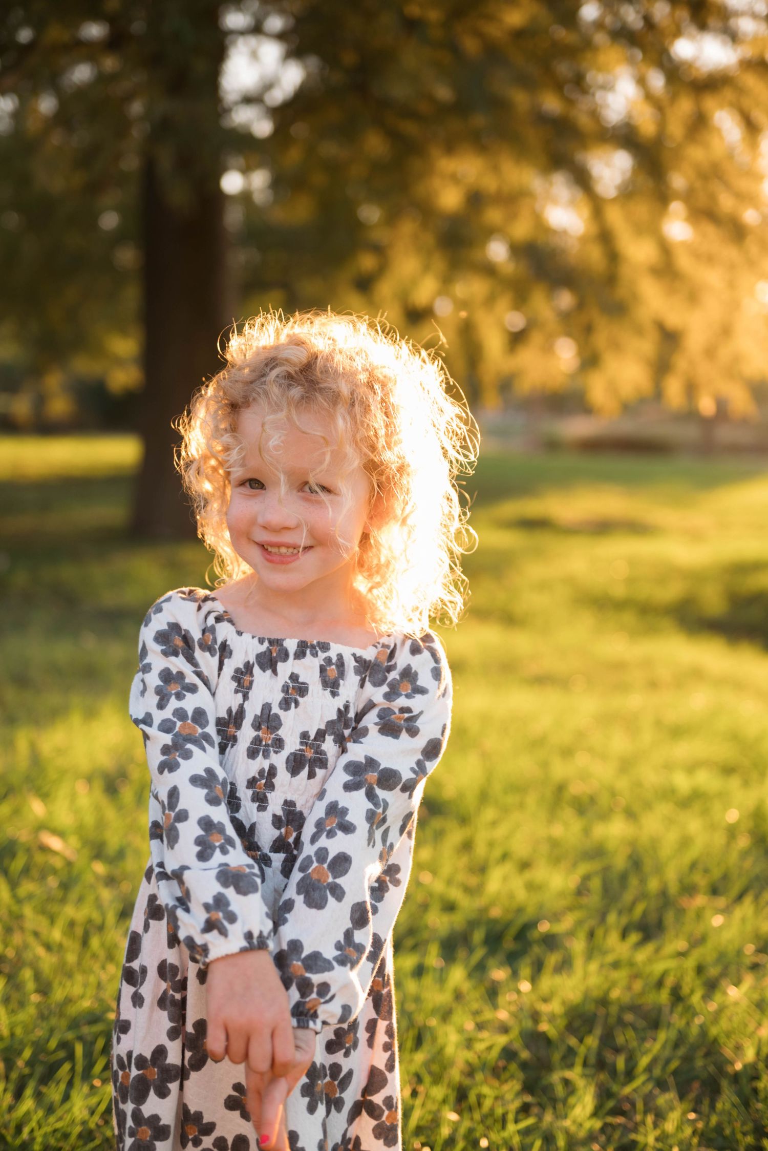 A child with curly hair backlit by golden sunlight plays in a grassy field during sunset.