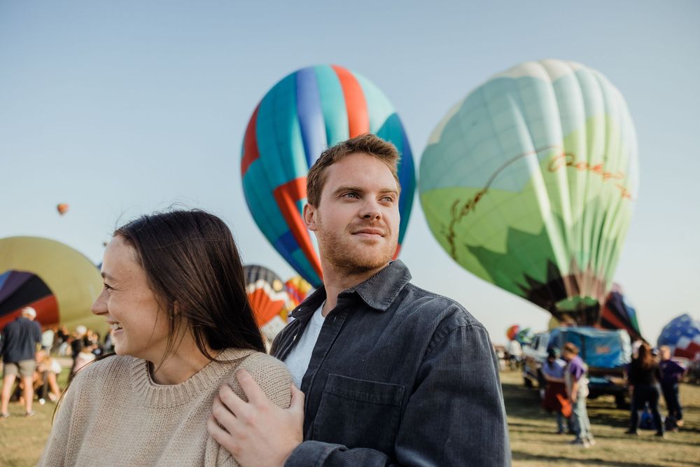 Happy couple standing together at hot air balloon festival with colorful balloons inflating behind them.
