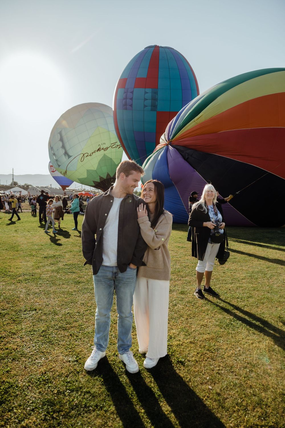 Happy couple standing close together at hot air balloon festival with colorful balloons being inflated nearby.