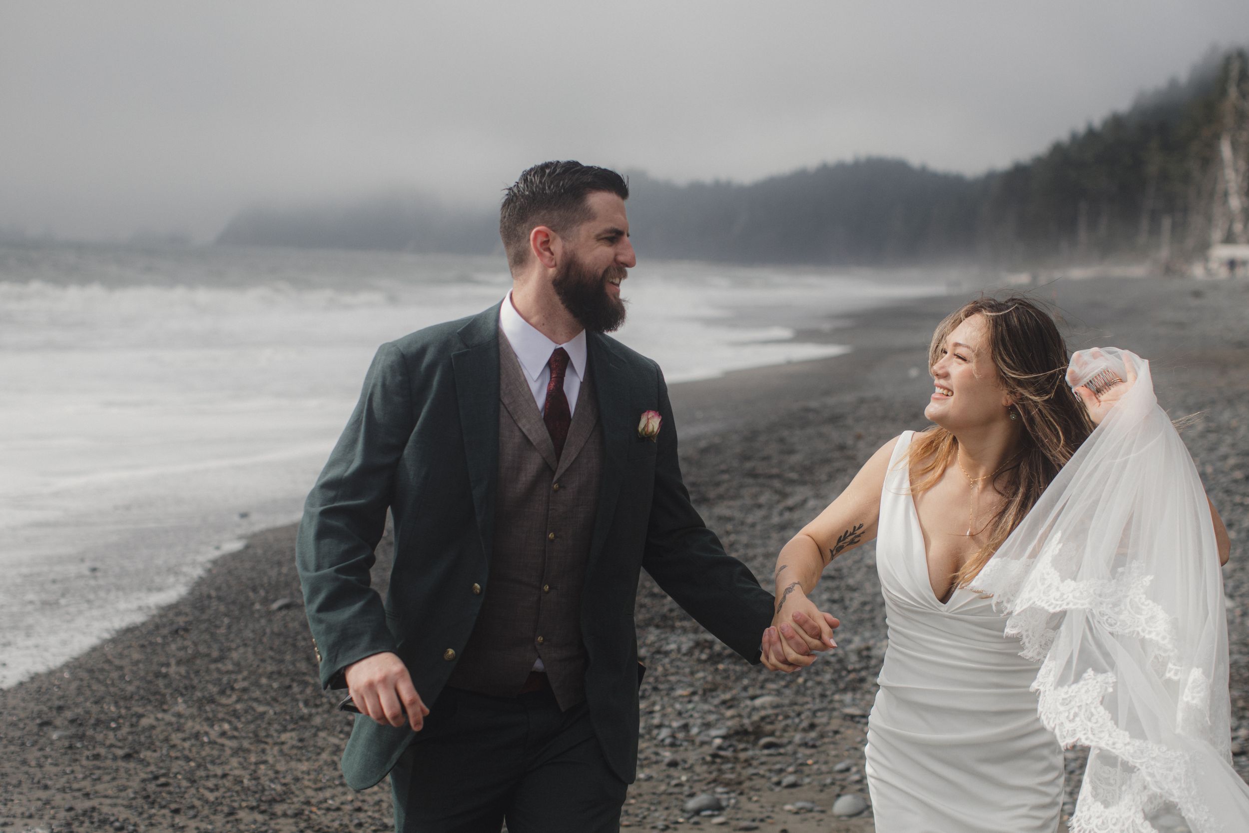 A couple share a joyful moment together on a misty rocky beach wearing wedding attire.