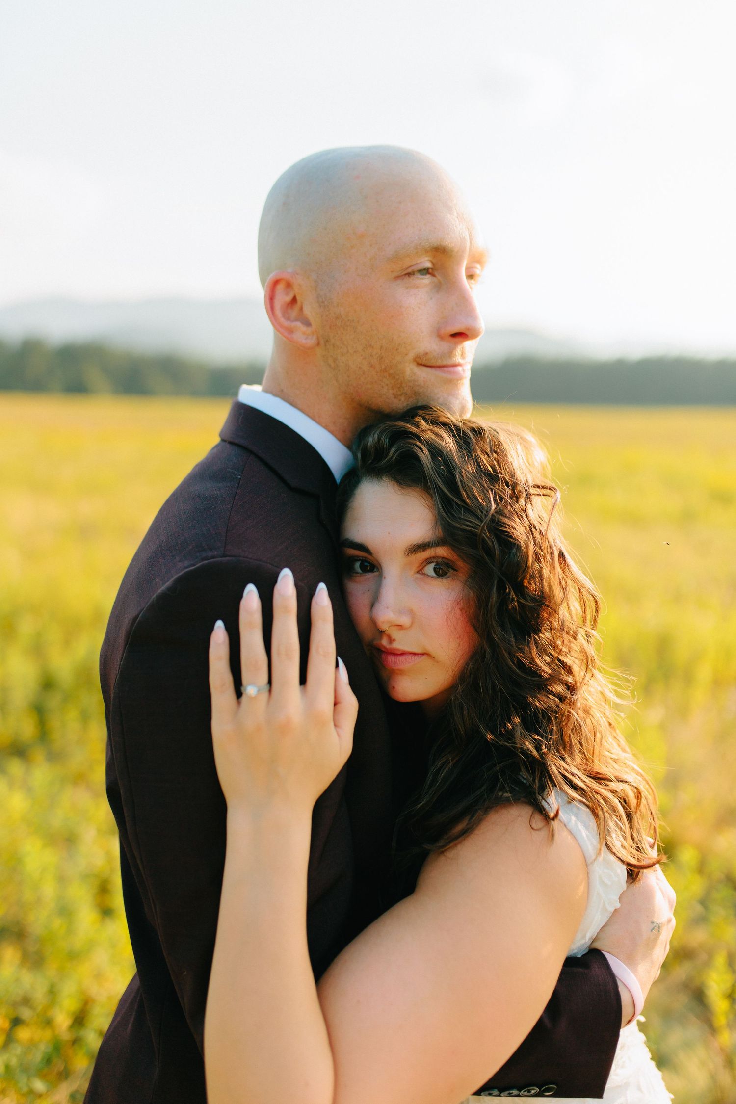 Romantic golden hour portrait session in a sunlit meadow with a couple embracing in formal attire.