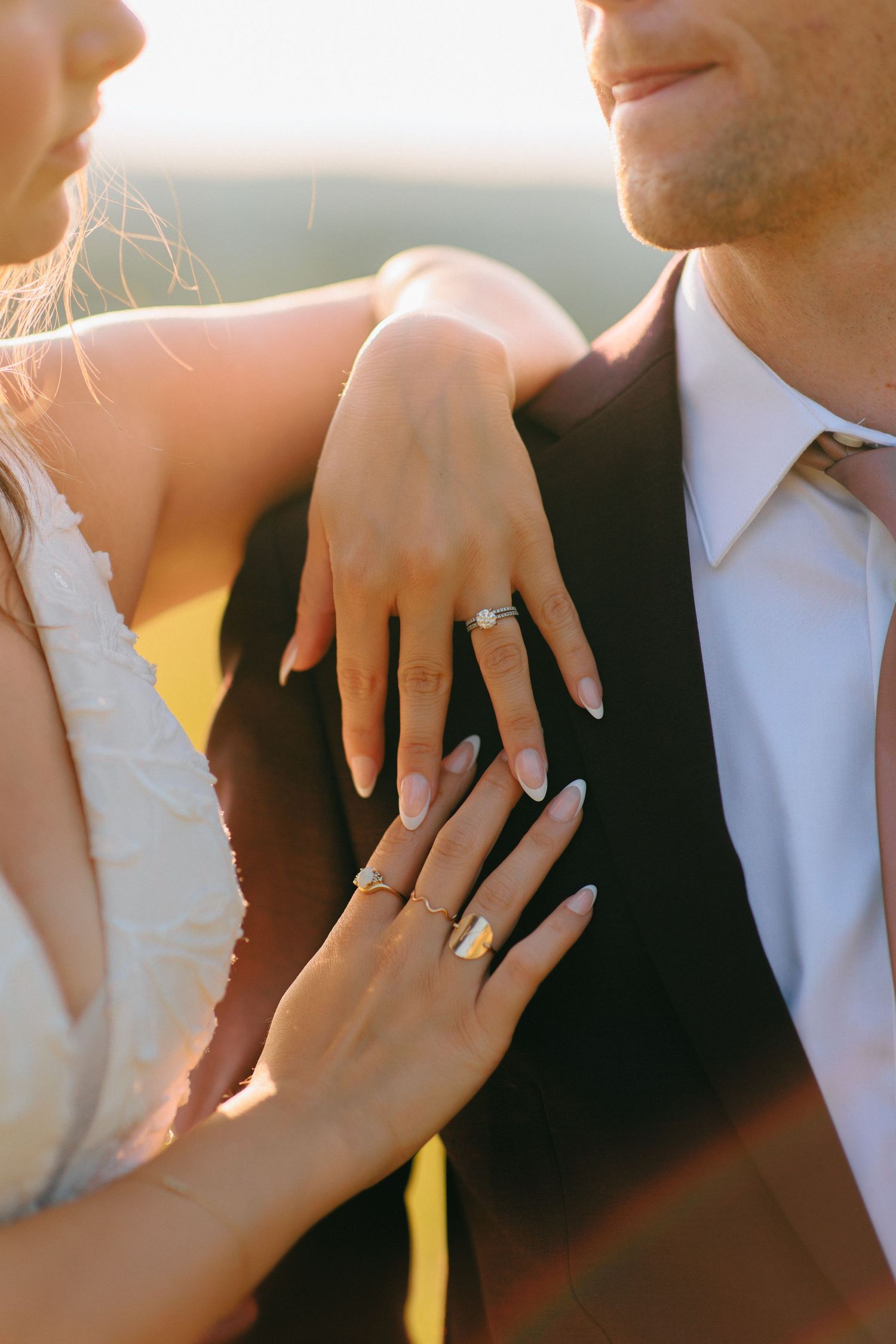 Close up shot showing wedding rings on hands against formal attire at sunset.