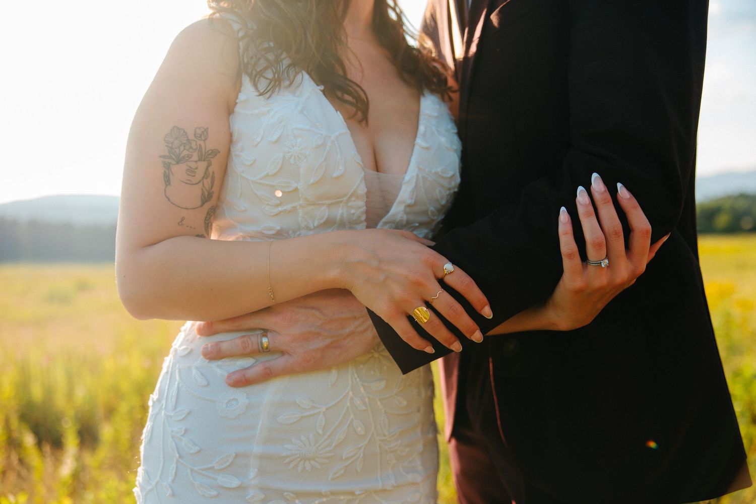 Couple in formal wedding attire embraces lovingly in a golden field during sunset.