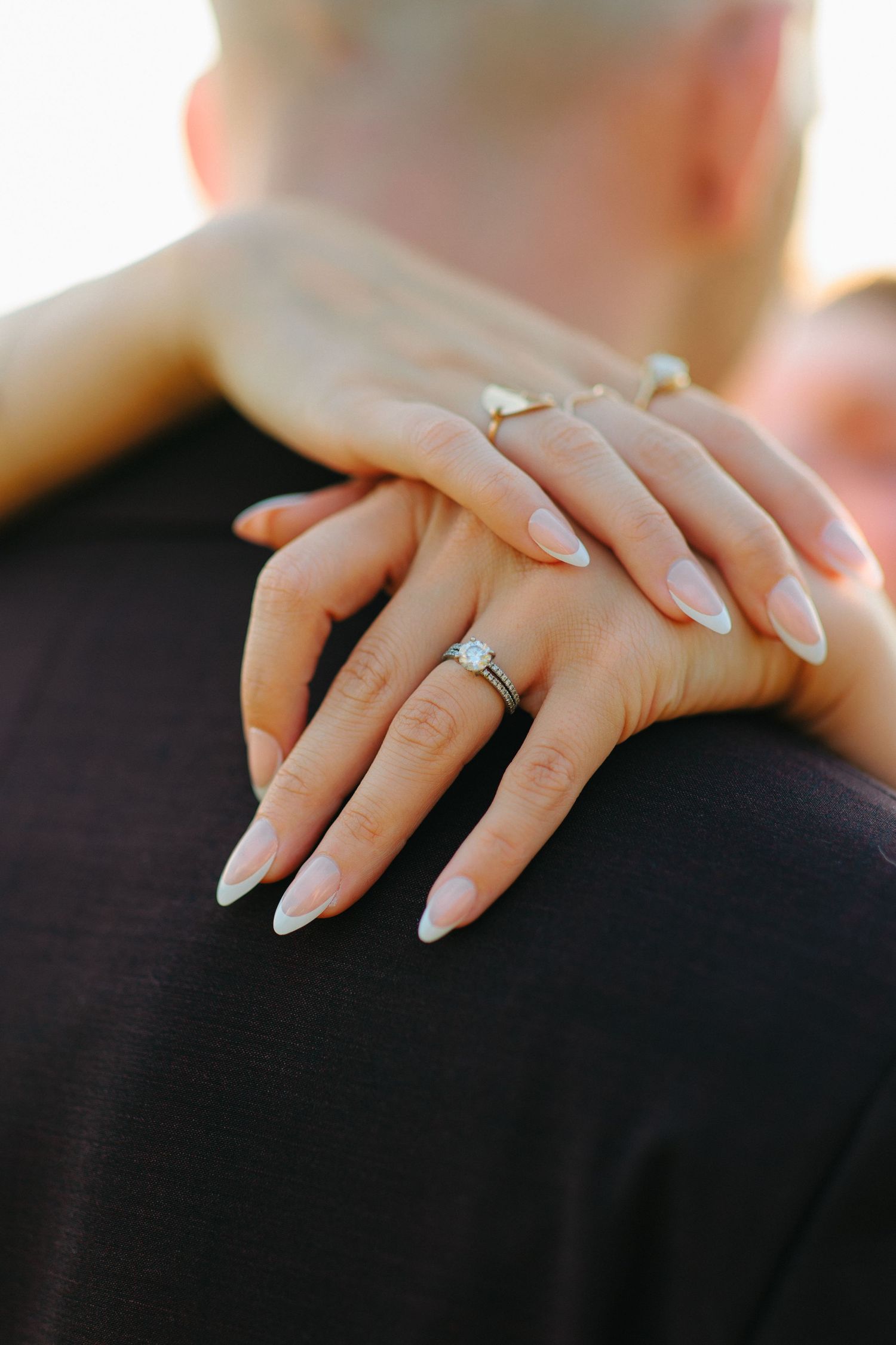 Close-up of manicured hands with long white acrylic nails resting on black fabric.