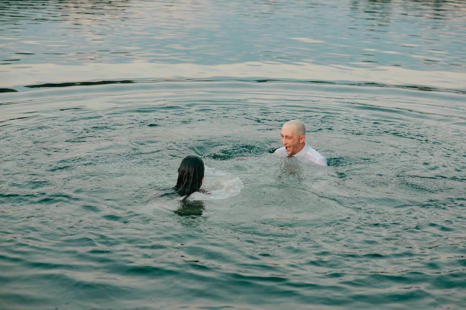 A black dog and person playing together in calm blue waters during a swimming session.