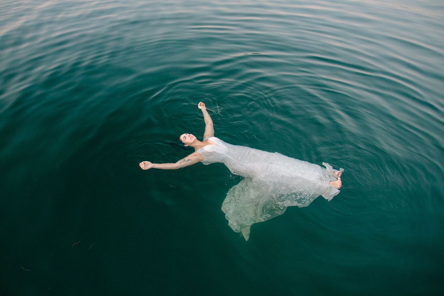 A person in a white dress floats gracefully in turquoise ocean waters, creating a dreamy underwater scene.