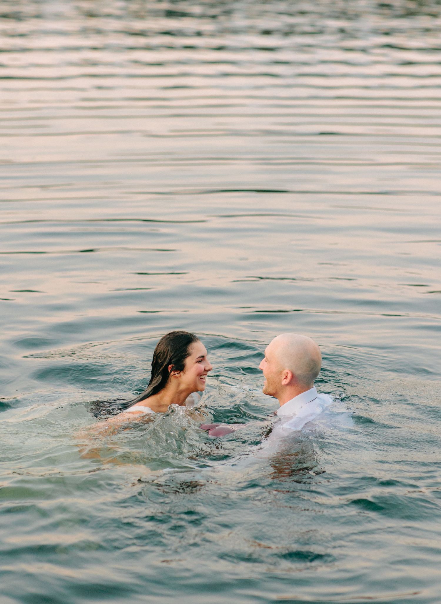 Happy couple playing in the water during their lakeside wedding photoshoot.