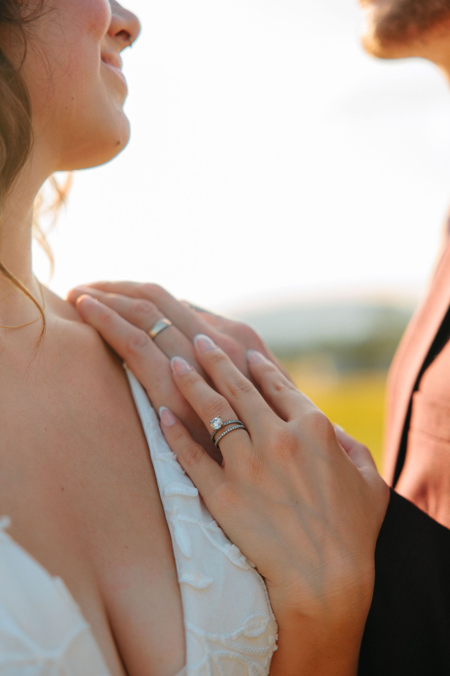 Close-up view of hands wearing wedding rings in golden sunlight against a white dress.