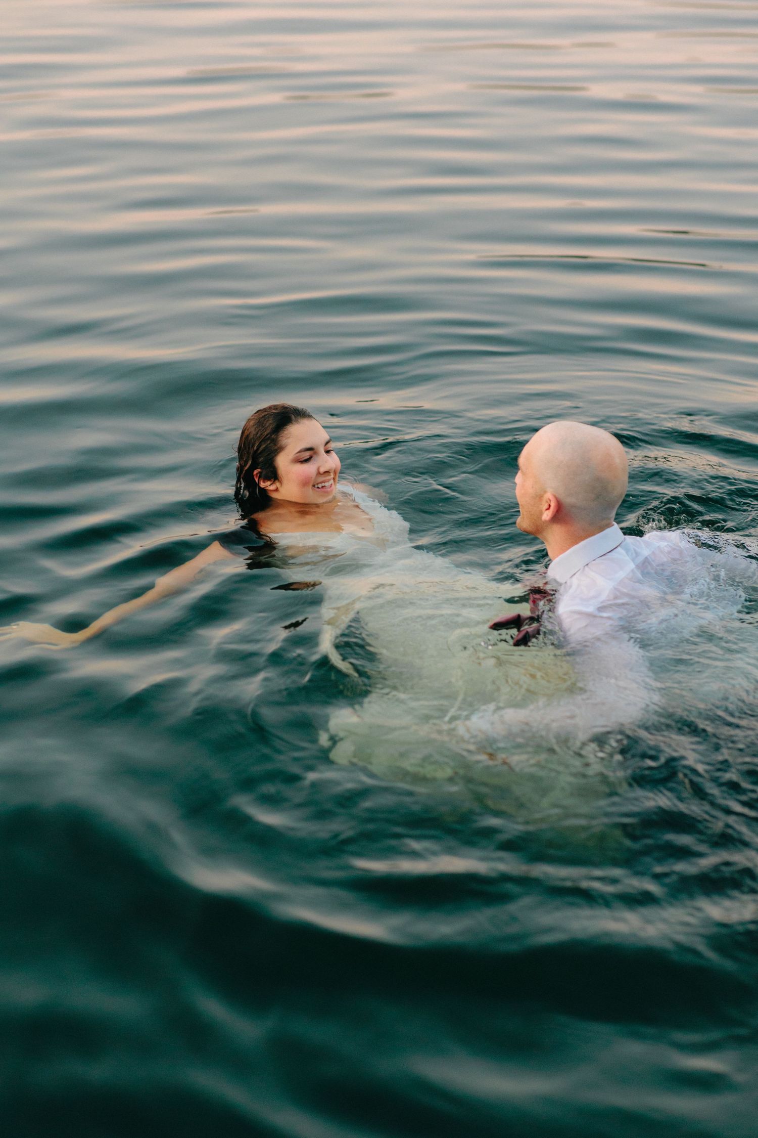 Sequence of two people swimming in calm ocean water at dusk.