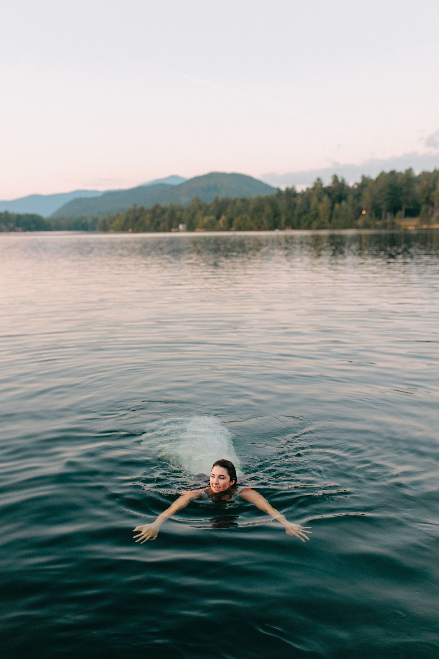 A person floating and swimming in a serene mountain lake with arms spread wide.