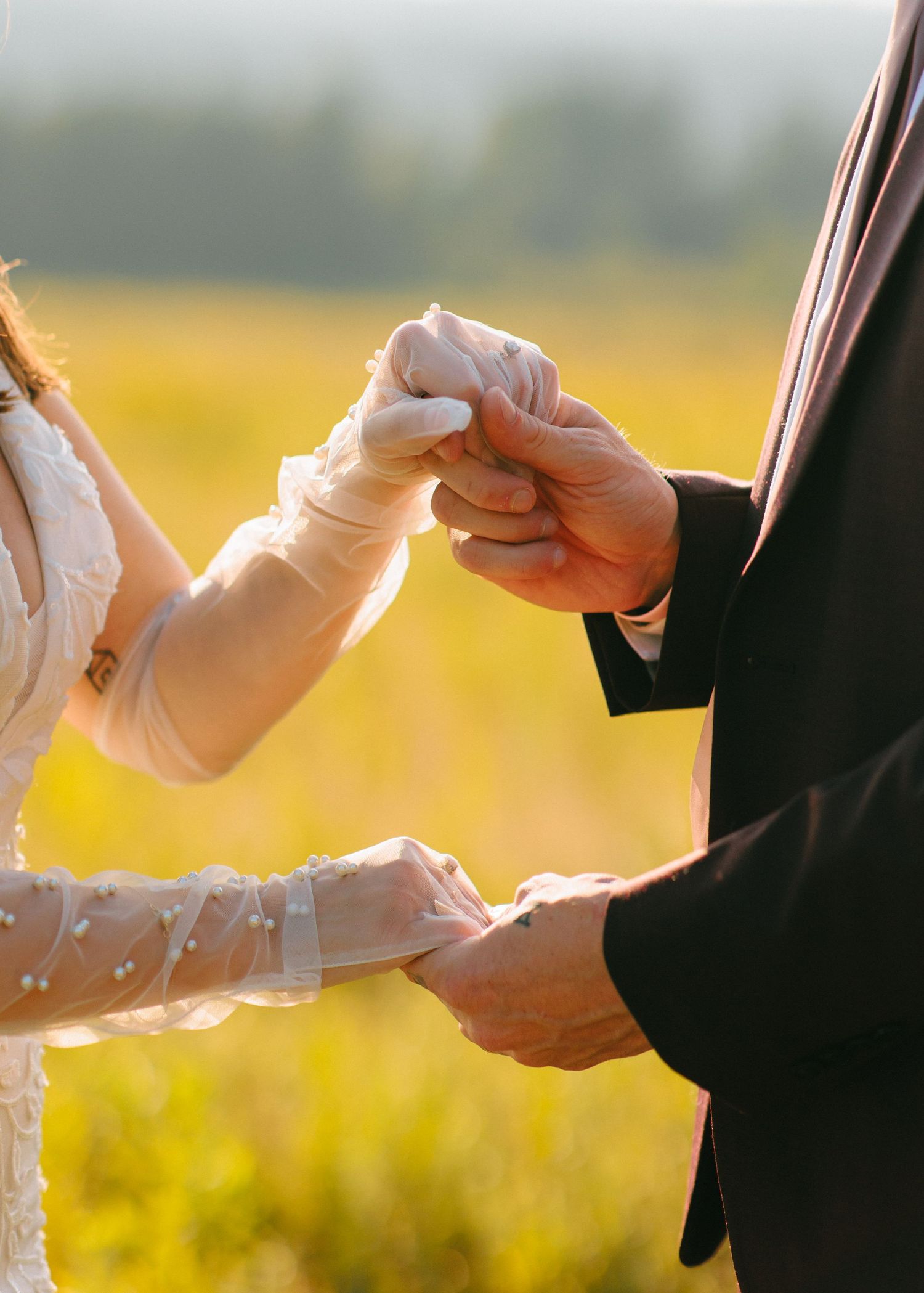 Couples hold hands in a chain during sunset wedding ceremony creating a unity symbol with golden light in background.