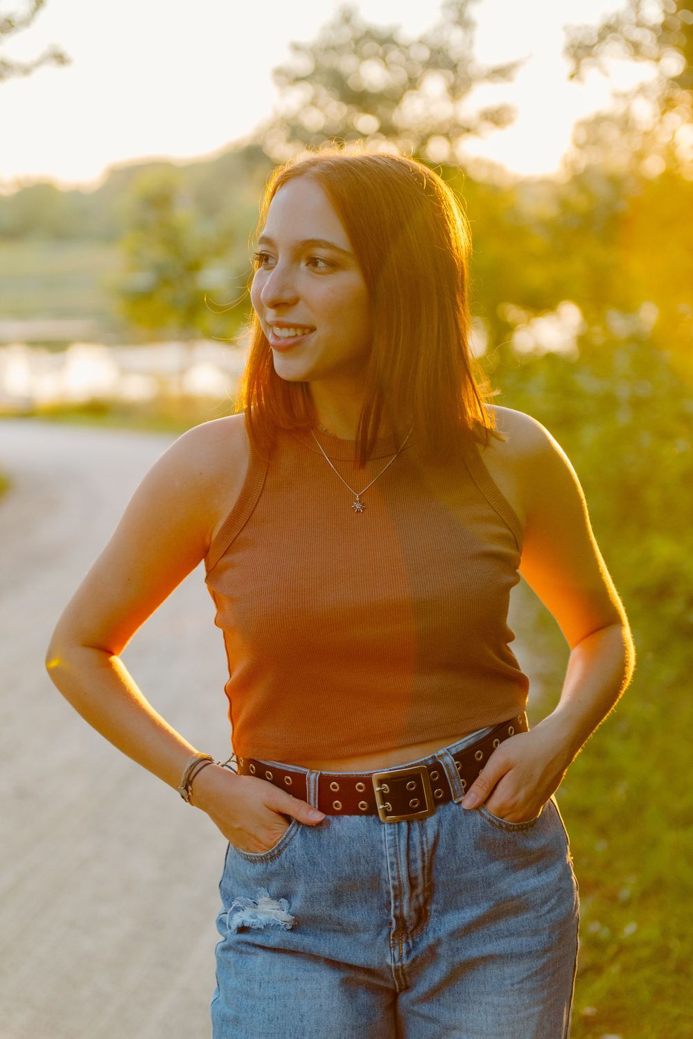 Woman enjoying golden hour sunlight wearing high waisted denim jeans and brown top in outdoor setting.