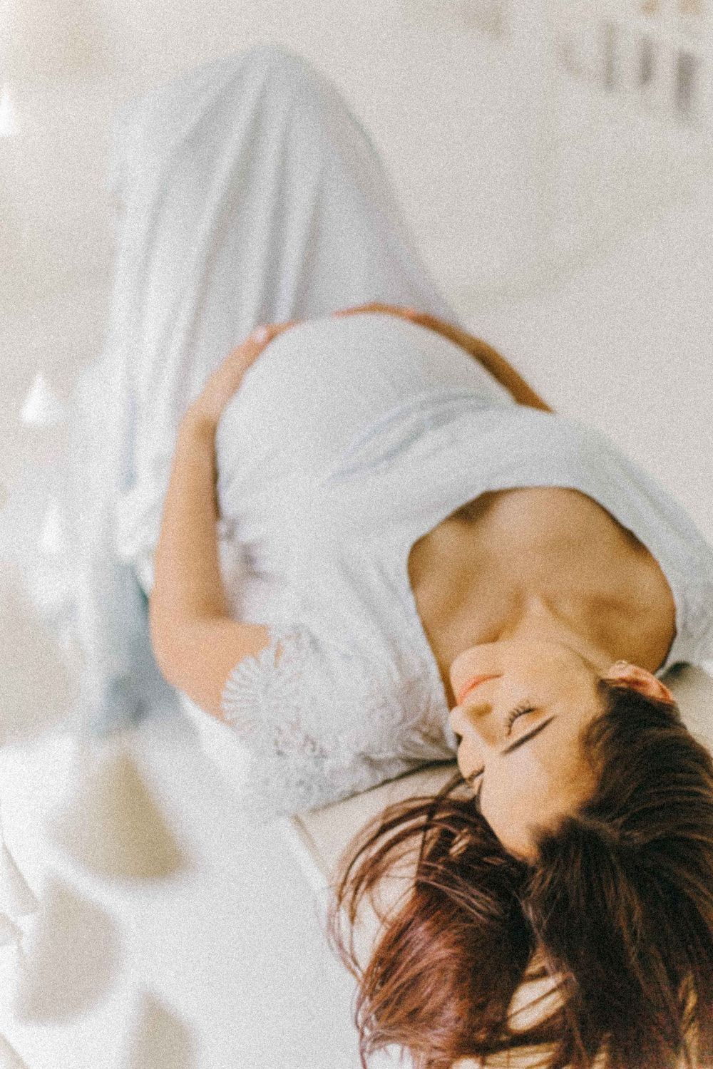 Artistic portrait of woman in white dress lying back in dreamy pose. Alenquer, Lisbon, and Portugal photography studio maternity session.