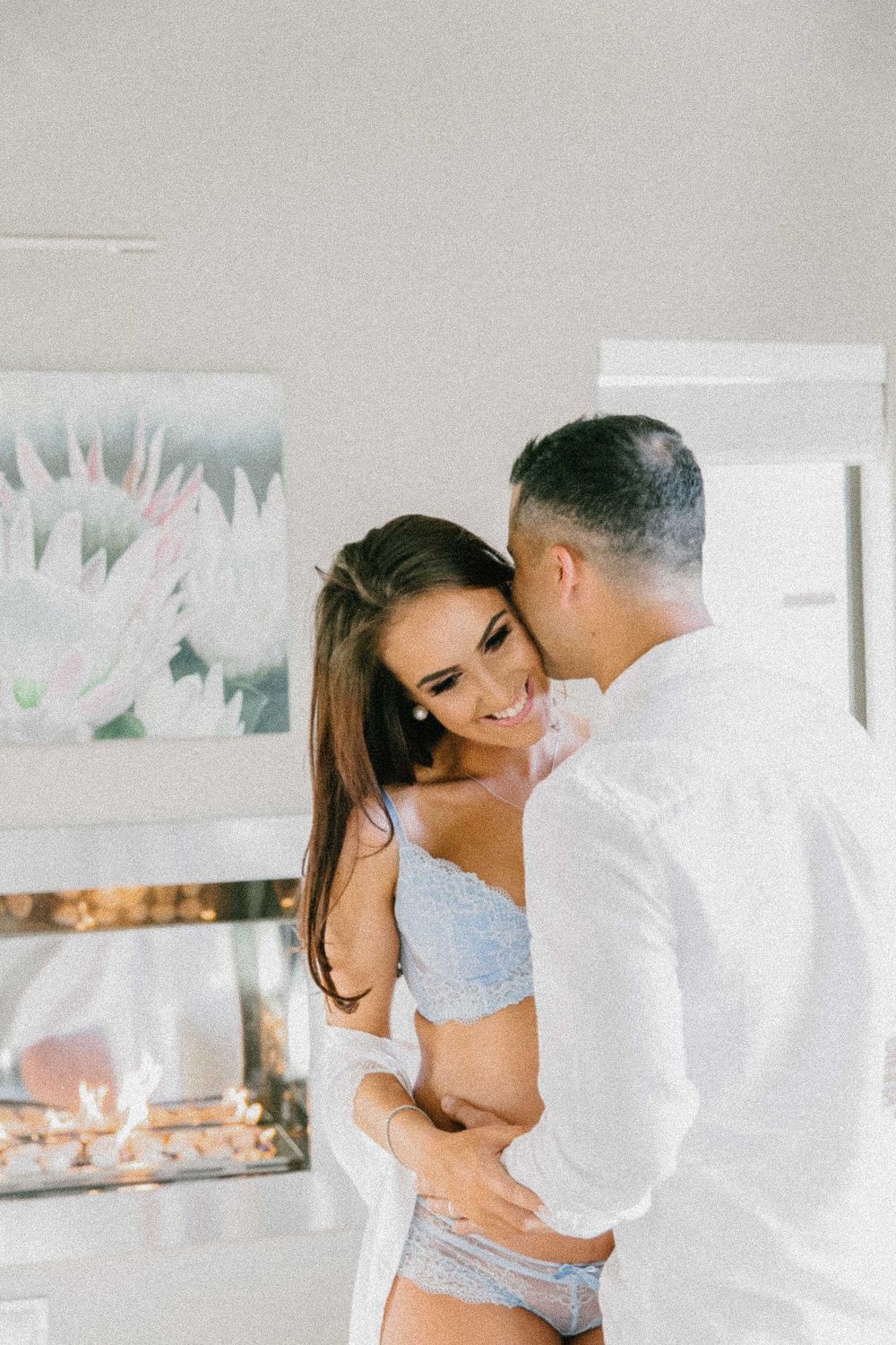 Intimate couple sharing a romantic moment in white and blue lingerie against a light background. Specializing in maternity, newborn.