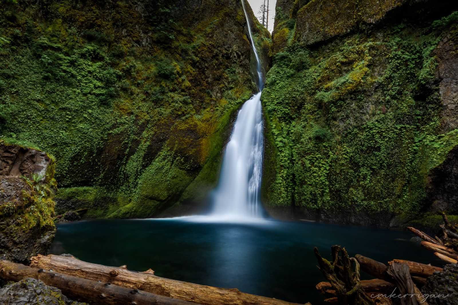 Long exposure waterfall cascades through moss-covered rocks in a lush green forest.