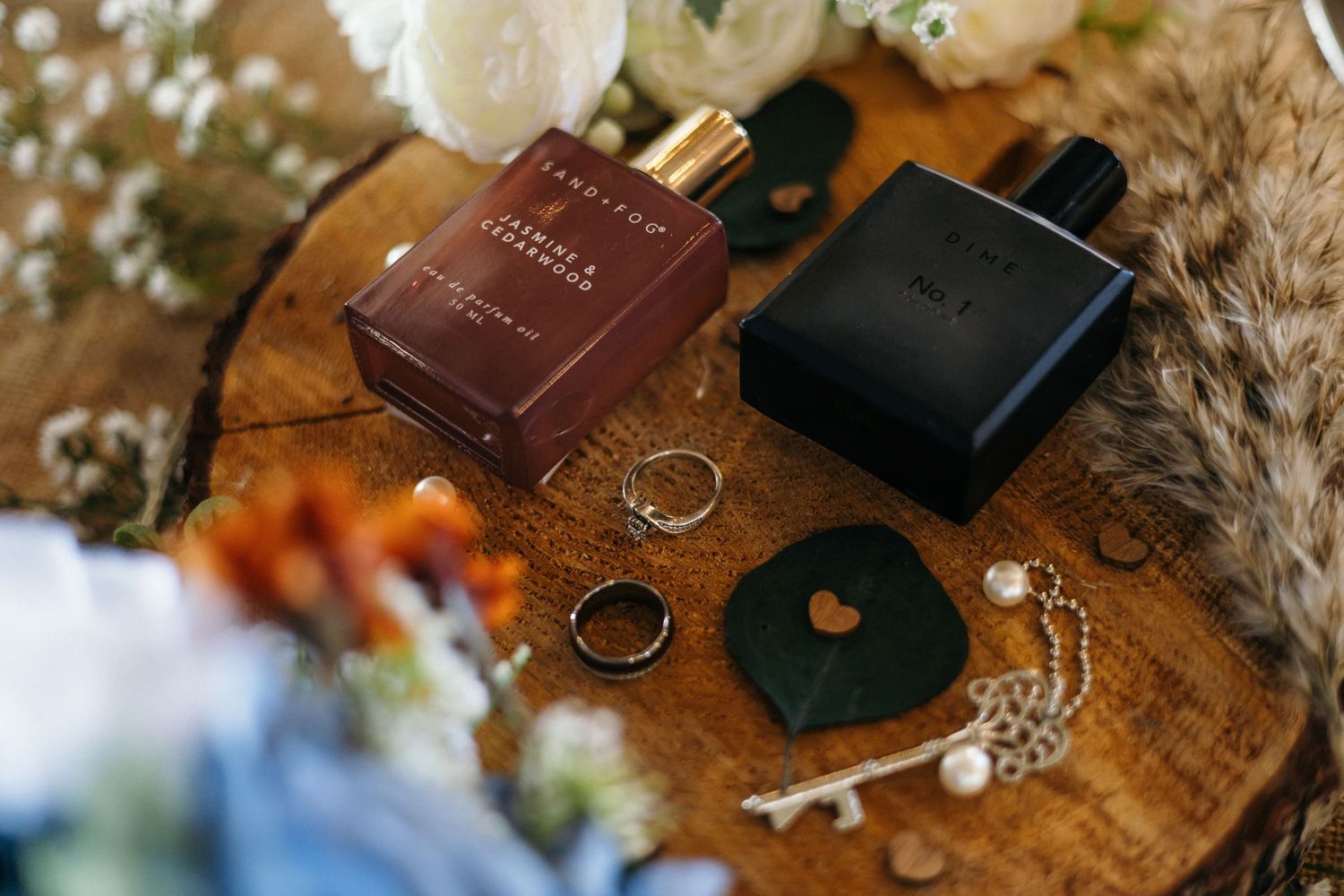 A black and white still life with wedding rings in a box, alongside jewelry and a sandal on a wooden surface.