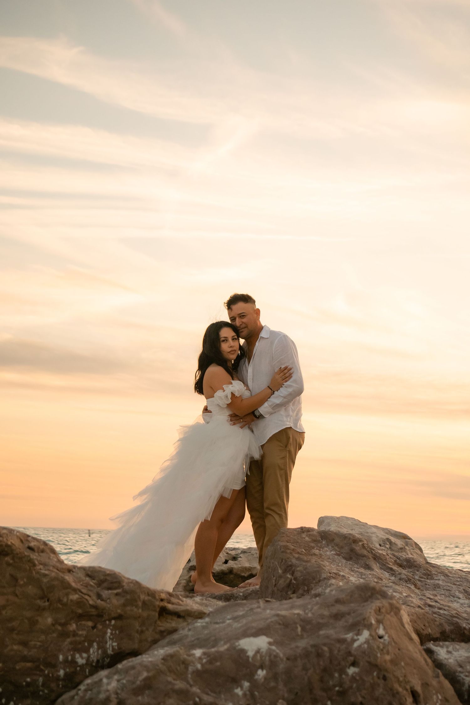 Romantic sunset photoshoot on rocky coastal cliffs overlooking the ocean.