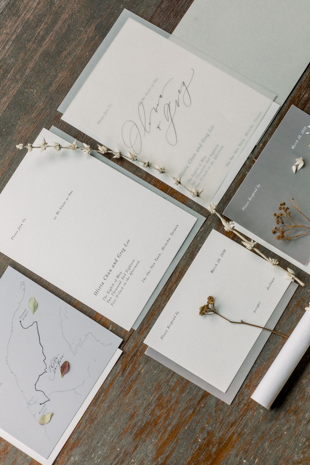 Minimalist wedding stationery suite with dried flowers and elegant calligraphy laid out on a rustic wooden surface.