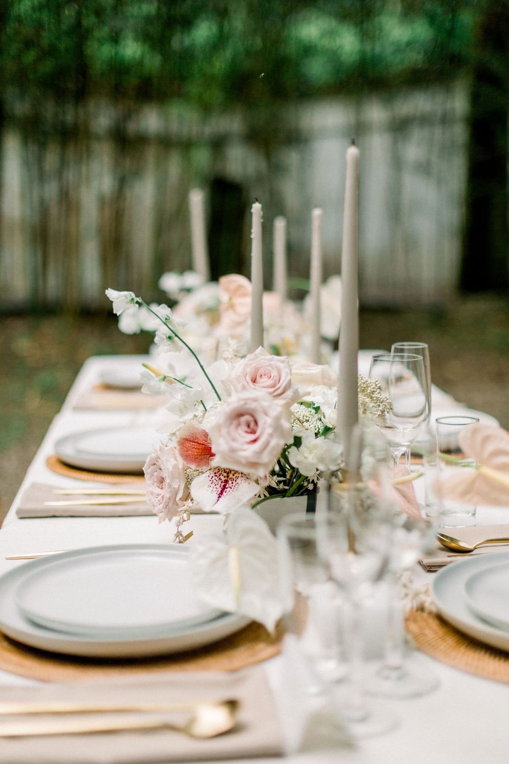 Elegant table setting with pink roses, white candles and place settings arranged on a rustic wooden surface.