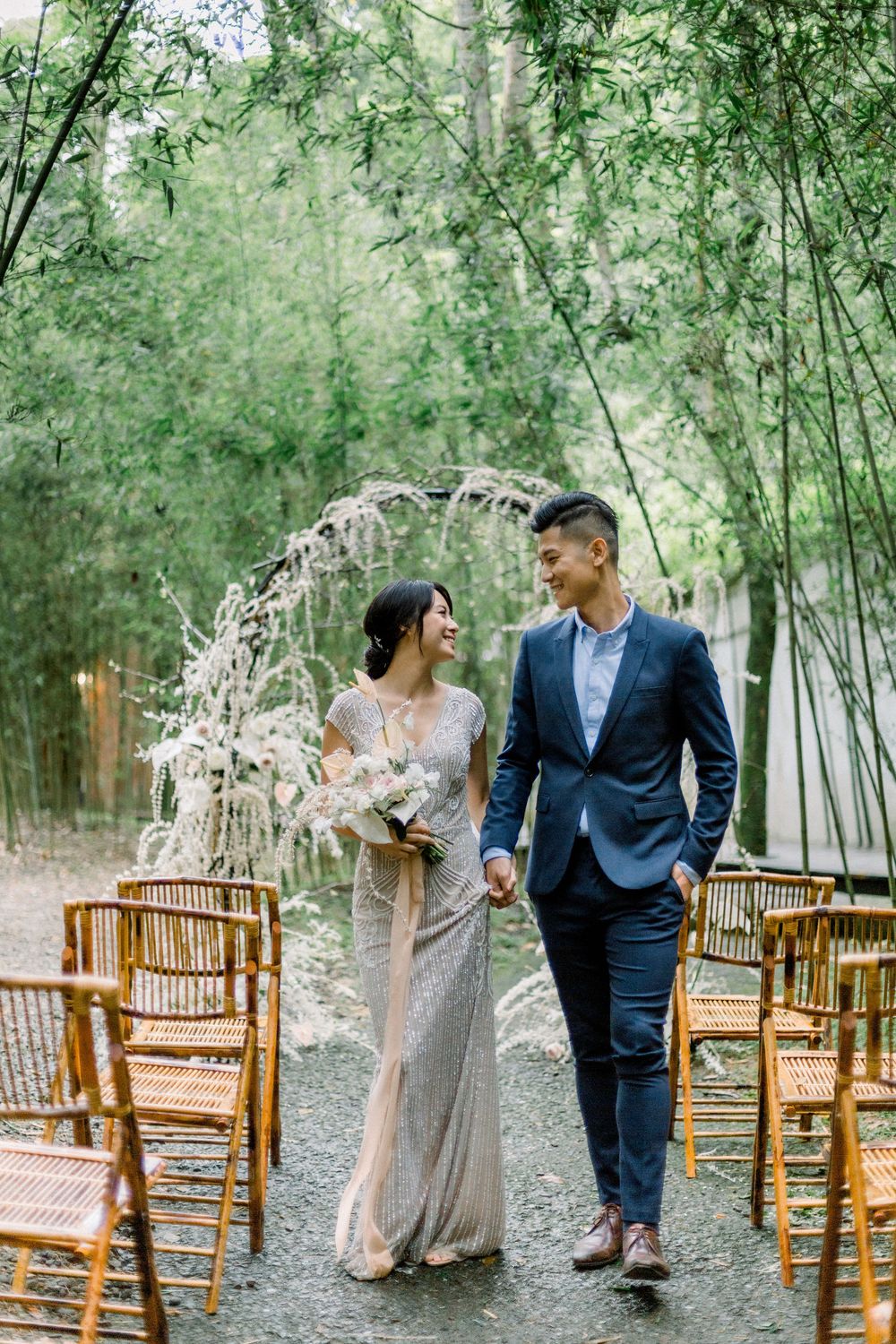 Romantic outdoor wedding ceremony setup with bamboo chairs and floral arch in a serene bamboo forest setting.