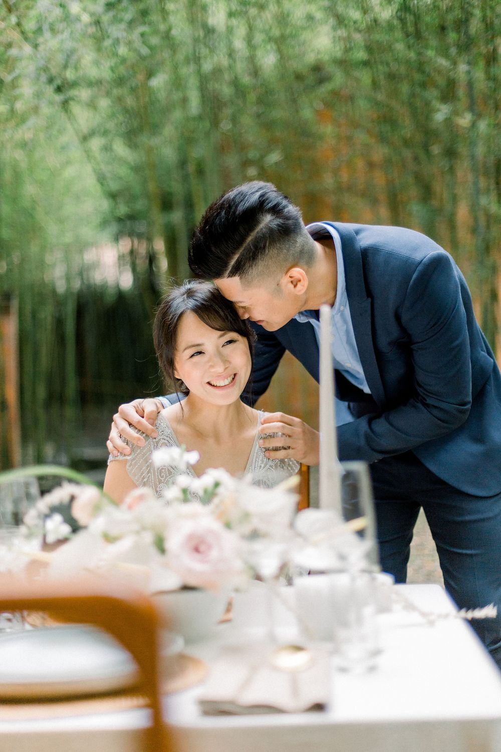 A couple shares intimate moments at an elegant table setting with bamboo forest backdrop.