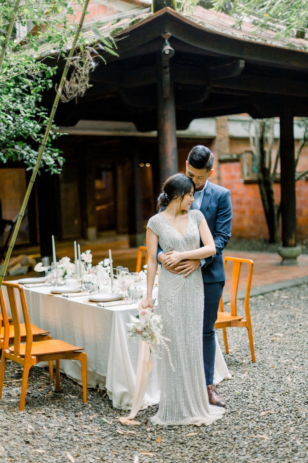 A romantic outdoor dining setup with wooden chairs and white table settings at a rustic venue.