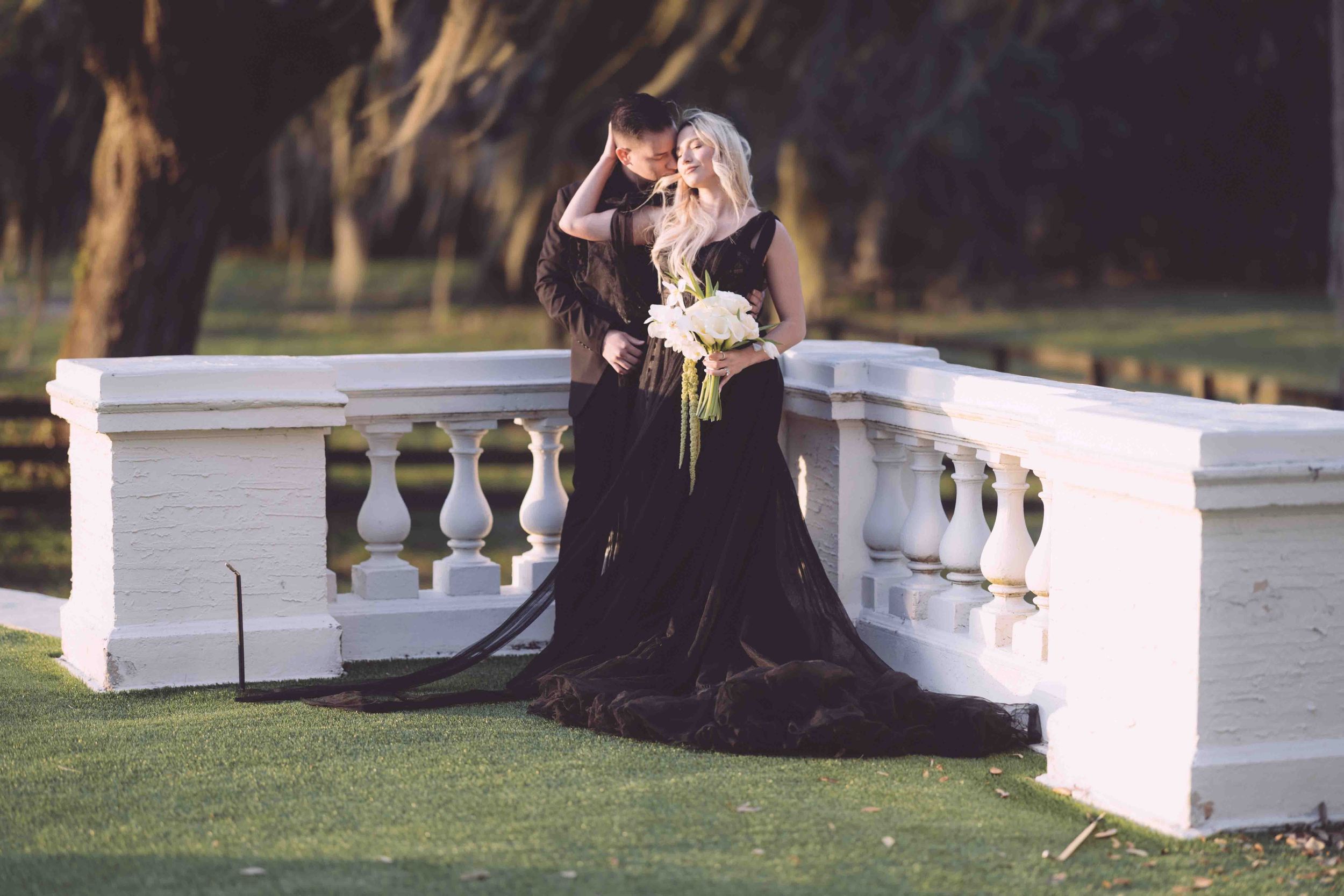 Wedding party sits on elegant white staircases in a scenic outdoor garden setting during sunset.