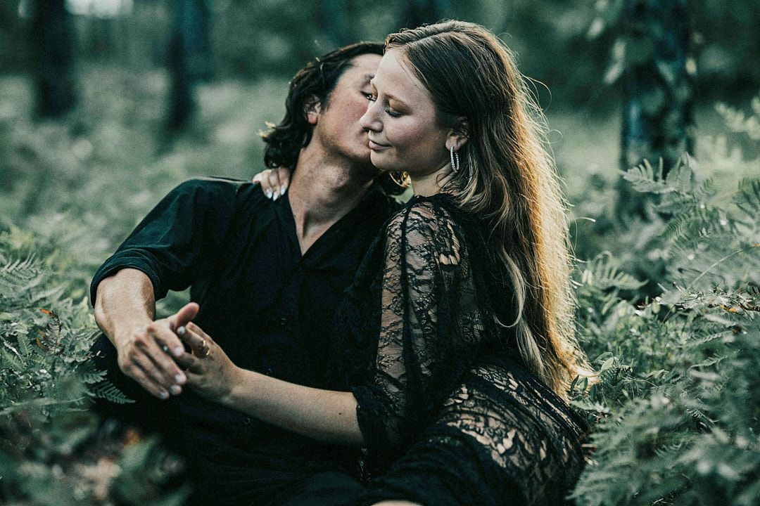 A couple embraces while sharing a romantic moment together in a moody forest setting with dark green foliage.