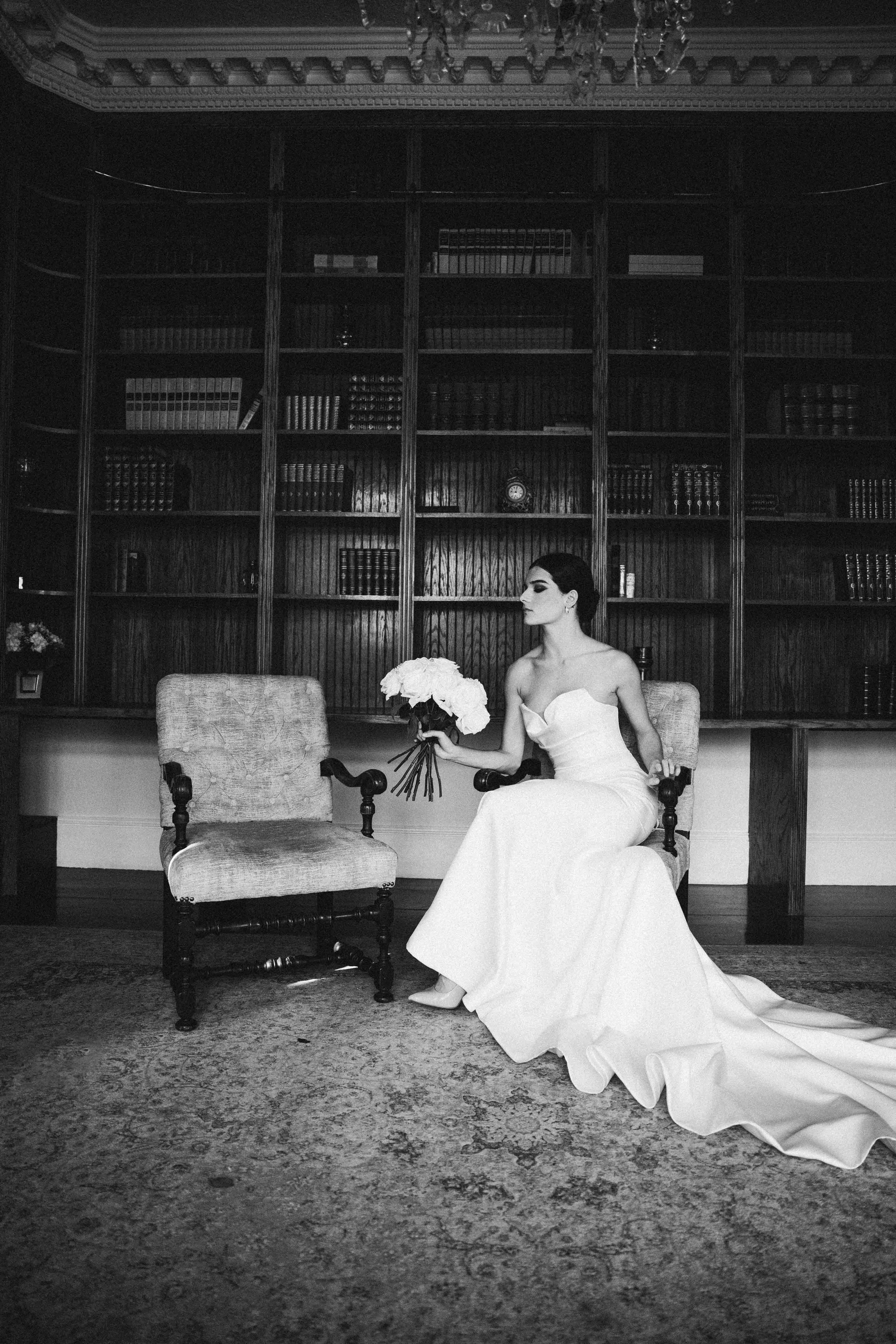 A series of black and white photos showing a person in a white wedding dress reclining on a library floor with bookshelves behind.