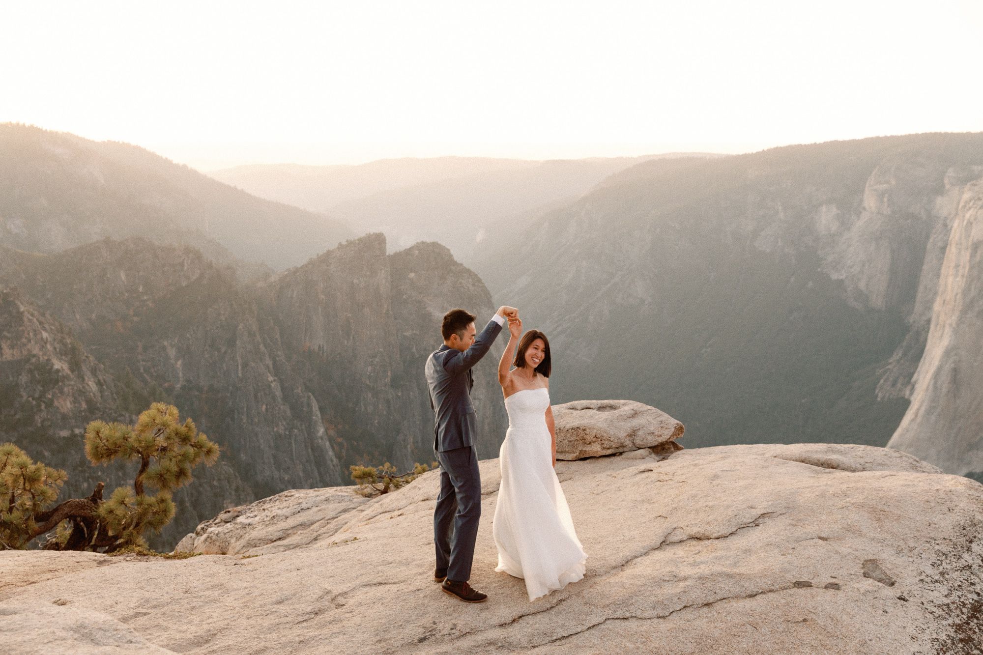 Groom spins bride on rocky Yosemite overlook during golden hour mountain elopement.