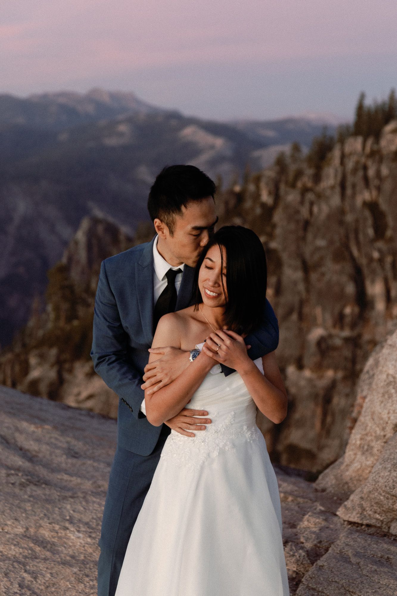 Groom embraces smiling bride at mountain summit during purple twilight elopement.