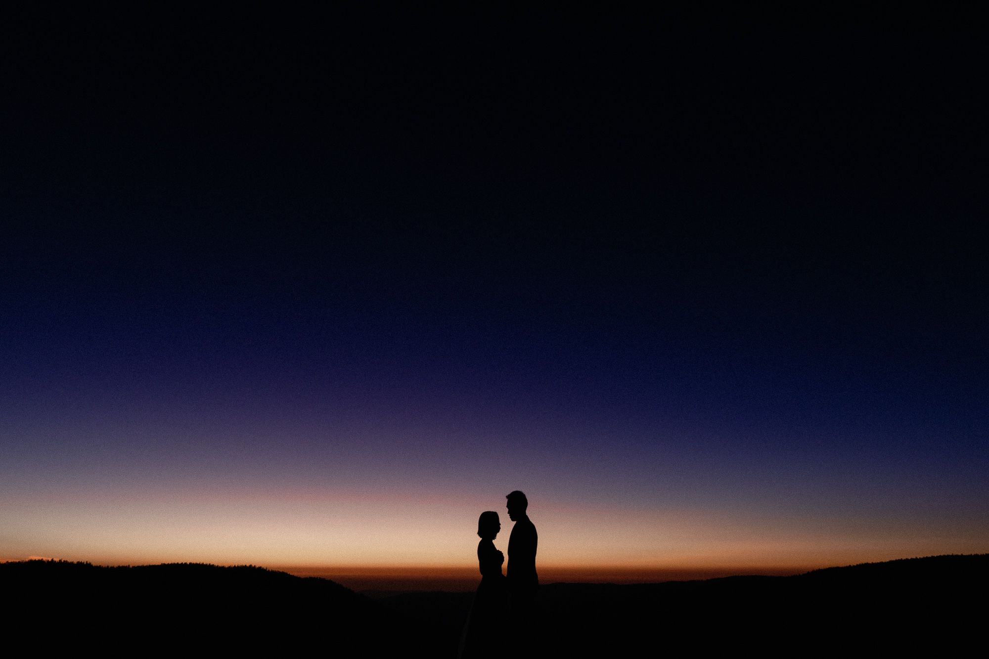 Romantic silhouette of couple facing each other against vibrant sunset gradient sky.