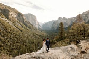 Bride and groom walk on granite rock with stunning Yosemite Valley tunnel view behind them.