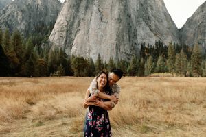 Couple embracing and laughing in a golden meadow with dramatic granite cliffs at Yosemite National Park.
