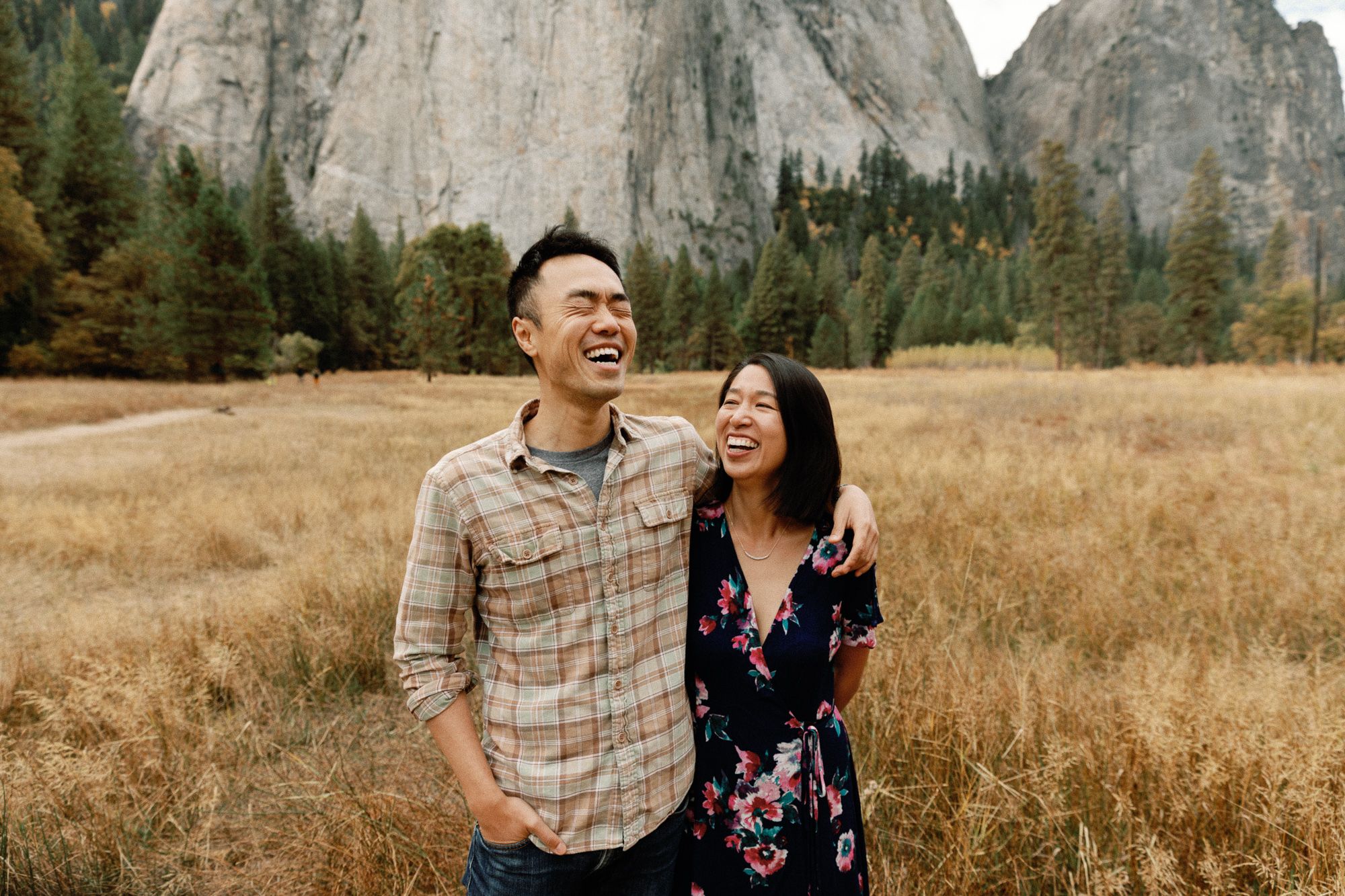 Happy Asian couple laughing together in a dry grass field with towering rock formations in Yosemite.
