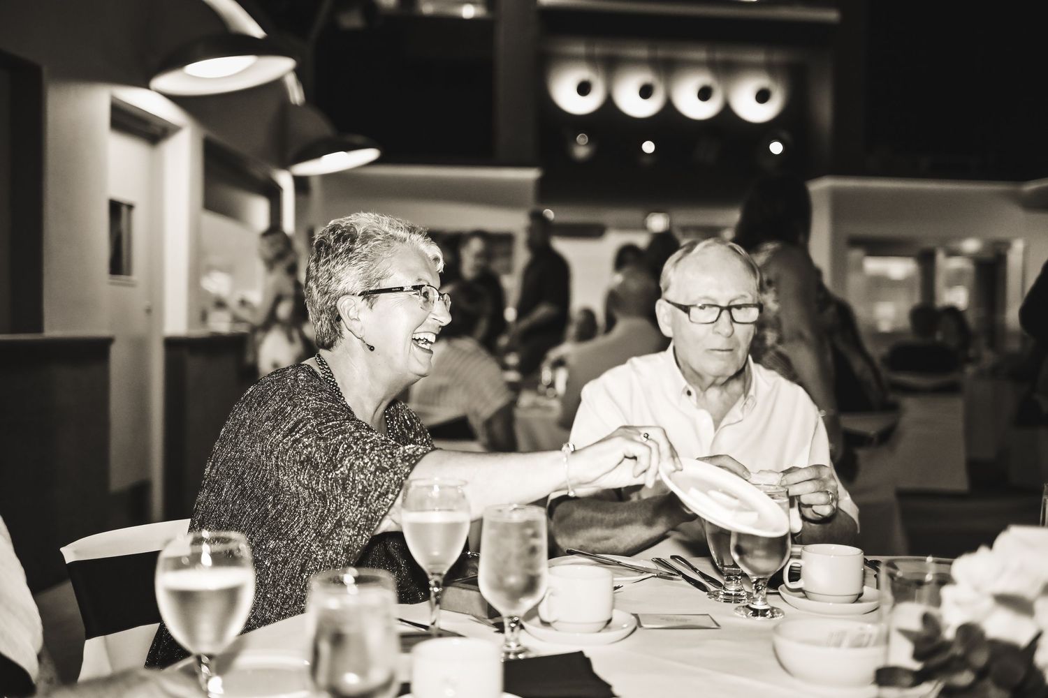 Black-and-white photo of a smiling man enjoying the wedding reception at his table.